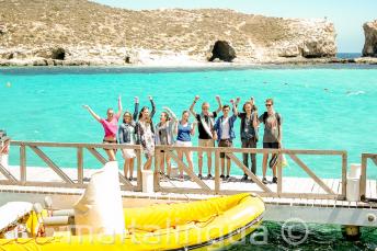 Bir grup ogrenci Comino'da Blue Lagoon'un kenarinda el salliyorlar