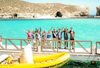 Bir grup ogrenci Comino'da Blue Lagoon'un kenarinda el salliyorlar